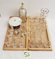 Overall view of vintage bar glassware on wooden trays, including soda siphon, various glasses, and pitcher.