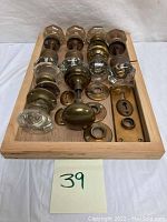 Top-down view of vintage glass and brass doorknobs arranged in wooden tray, showing multiple knobs and brass hardware pieces.