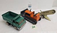 Set of three vintage Structo pressed steel metal toy vehicles: dumper truck, dozer, and sand loader, with scale reference bottle and lot number card.
