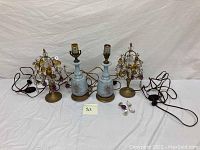 Photo showing all four lamps: two with blue Bristol glass bases with floral motifs and two brass lamps with hanging colored glass prisms.