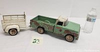 Vintaged pressed steel Tonka Campa green pickup truck with white cab roof and matching white trailer, both showing rust and paint wear, displayed next to a water bottle for scale.