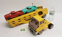 Front and side view of the yellow vintage Tonka truck car hauler with turquoise and red plastic cars loaded on the trailer, water bottle for scale.