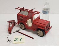 Photo showing the full red Tonka fire jeep metal toy with white seats, metal ladder on top, front hook, rod, and wrench accessories, alongside a water bottle for scale.