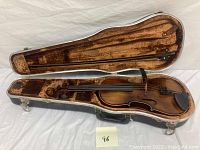 Violin in open hard case with bow inside, showing light brown varnish and fitting interior.