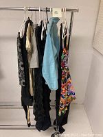 Overview of seven garments hanging on rack including skirts, tops, blouse, dress, and sweater