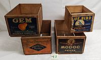 Five vintage wooden fruit crates arranged in two stacks, showing colorful branded labels for different pear brands and types.