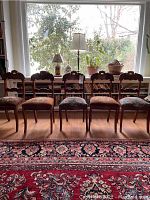 Six carved wood chairs arranged in a row in front of a window