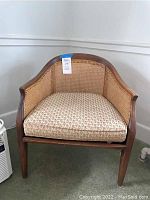 Wooden armchair with caned back and sides, featuring a removable floral patterned cushion.