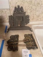 Full view of the fireplace fixtures comprising the central decorative backplate showing lion and unicorn motif, two decorative side panels, and three metal rods.