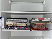 Books on white shelf including large books on textiles, quilting, basketry, and some regional histories or artistic topics.
