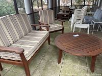 Two-seat bench and one armchair facing a round slatted wood table