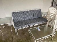 Full setup showing iron glider sofa with striped cushions, matching tables, and stacked resin chairs.