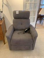 Front view of gray lift chair showing tufted back, padded armrests, and wired remote on seat