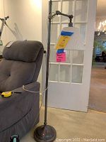 Full view of the lamp beside a sofa showing the overall height of approximately 56 inches and adjustable arm holding a pleated lampshade.