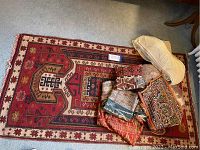 Overall view of red geometric rug with assorted textiles piled on one end