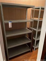 Two gray metal shelving units placed side by side in a wood-paneled closet showing 4 shelves each.