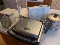 Lot items displayed on kitchen counter including American Family scale, Krups slicer, Breville pressed grill, bamboo steamer and double boiler.