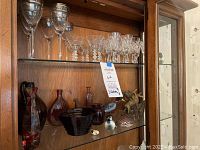 Wine glasses, aperitif glasses, animal figurines, and vases displayed on wooden shelving.