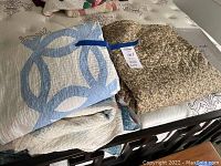 Multiple folded hand-made quilts displayed on a bed, including a blue and white interlocking ring design and a floral patterned quilt.
