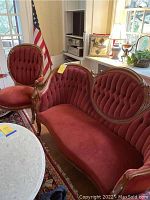 Wide view of red velvet tufted settee alongside matching rocker chair in room.