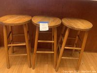 Front view showing all three wooden bar stools placed side by side with round seats and four legs each.