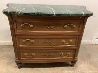 Front view of antique wooden chest with green marble top, showing three drawers with brass handles and decorative keyholes.