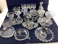 Full lot view showing assorted glassware pieces including stemmed glasses, bowls, trays, and serving dishes arranged on dark cloth background.