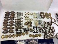 Top-down view showing organized groups of drawer pulls, knobs, hinges, ceramic handles, and door hardware pieces, all used and mostly metal with varying finishes.