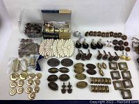 Wide view of assorted hardware organized on a flat surface including drawer pulls, doorknobs, casters, and hooks.