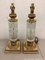 Pair of brass and glass table lamps showing cut glass cylindrical bodies and ornate brass square bases.