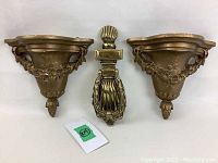 Front view of brass door knocker lying between the two wood wall mounted brackets, all with a metallic finish.