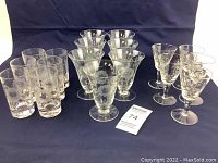 Full view of the 18 glass pieces arranged on a dark background showing the different sizes and shapes with cornflower etching.
