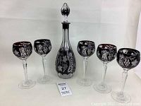 Group photo showing decanter with stopper and six matching stemmed glasses on white background.