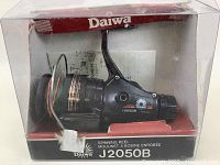 Daiwa J2050B spinning reel in clear view inside original packaging with branded box visible.