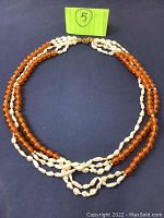 Full view showing a three strand necklace with two strands of small off-white freshwater pearls alternating with one strand of round orange beads.