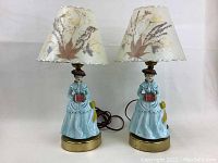 Pair of vintage figurine lamps with floral print shades, showing overall appearance and detail of the figurines and bases.