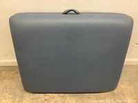 Closed portable massage table showing blue padded vinyl exterior with black integrated carrying handle on side.