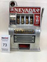 Front view of vintage toy slot machine showing 'NEVADA' text, coin slot, reels, and lever.
