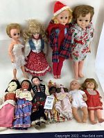 Photo showing all 10 dolls arranged on white background, various sizes and outfits visible, dolls range from porcelain to vinyl and fabric, some have damaged eyes