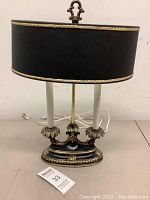 Front view of lamp with black oval shade, dual candelabra arms, and ornate black and gold base
