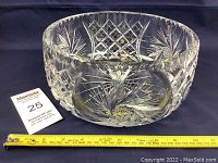 Photo showing the front side of a clear vintage cut crystal bowl with intricate starburst and diamond cut designs, and a yellow measuring tape indicating size.