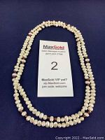 Full view of double-strand freshwater pearl necklace with occasional red beads laid flat on a dark blue background with a MaxSold label.
