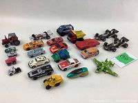 Top-side view of the full lot showing 22 vintage toy vehicles including race cars, trucks, and an airplane in various colors with some wear and paint loss.