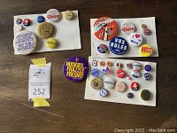 Overview of 38 miscellaneous vintage political, sports, and union buttons and pins arranged on multiple white cards and placed on a wooden surface.