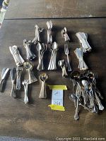 Overview of assorted flatware arranged on a table showing bundled forks, spoons, butter knives, a button hook, and berry spoons.