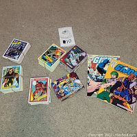 Overview of all comic magazines and trading cards included in the lot placed on floor. Two G.I. Joe comic magazines and multiple different bundles of trading cards are visible.