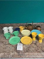 Full view of all items arranged on counter including 2 copper kettles, multiple colored Fiesta plates and egg cups, and white espresso cups.