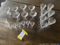 Full view of 21 crystal glasses arranged on a wooden surface, showing parfait, cordial and low sherbet glasses in matching style and design.