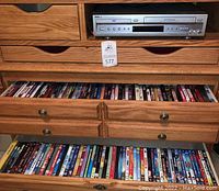 Sony DVD/VHS player on top of wooden furniture with open drawers filled with DVDs visible