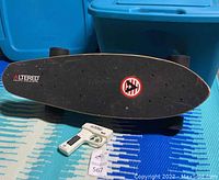 Full view of Altered electric skateboard laying on a patterned blue floor with wireless remote control placed in front of it.